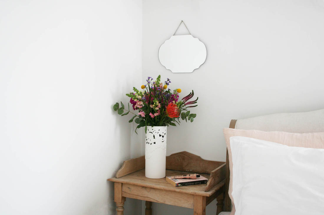 Minimal white bedroom with accents of dusky pink and vintage bedside table and mirror